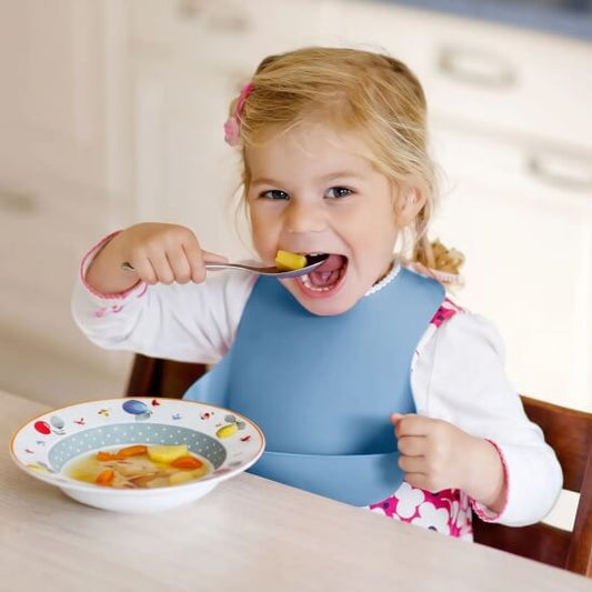 Fillette qui qui porte le bavoir bébé bleu et qui mange des fruits