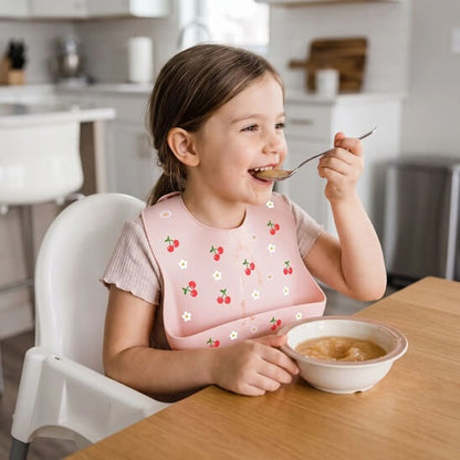 Fillette portant un bavoir bébé cerises qui mange de la compote