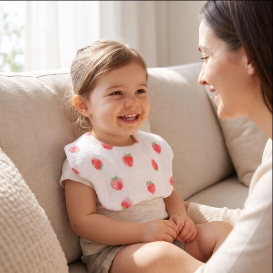 Fillette avec le bavoir bébé fraises assise sur un canapé