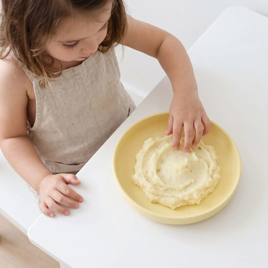 Fillette qui mange avec ses doigts assiette bébé jaune