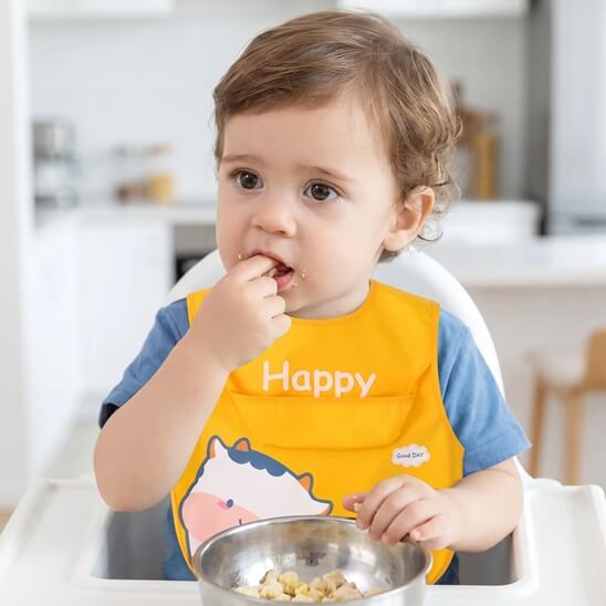 Garçon qui mange avec les doigts avec le bavoir bébé jaune