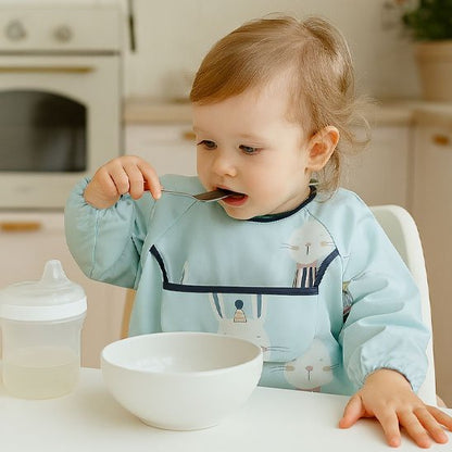 Fillette qui mange à la cuillère avec bavoir bébé lapin